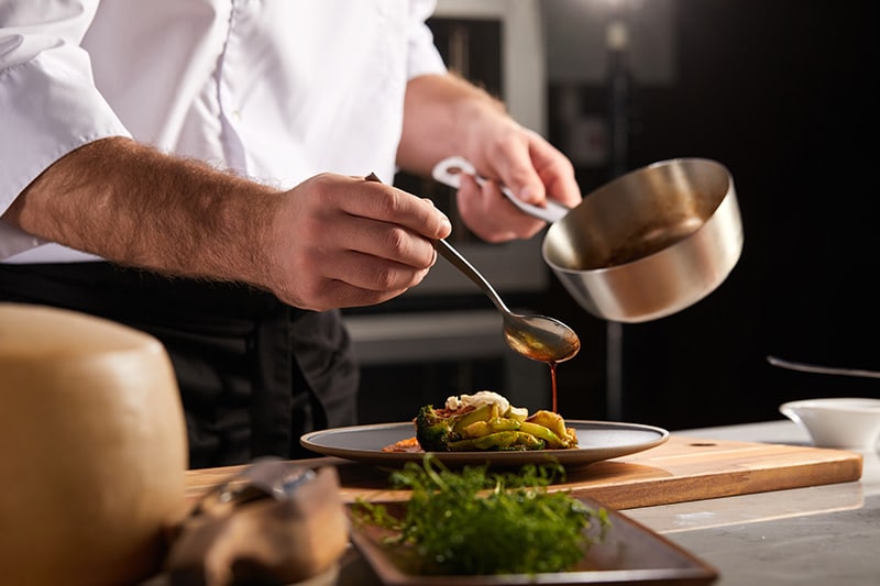 A food services industry worker, one of the jobs with the highest rates of addiction, tops a restaurant dish with a sauce.