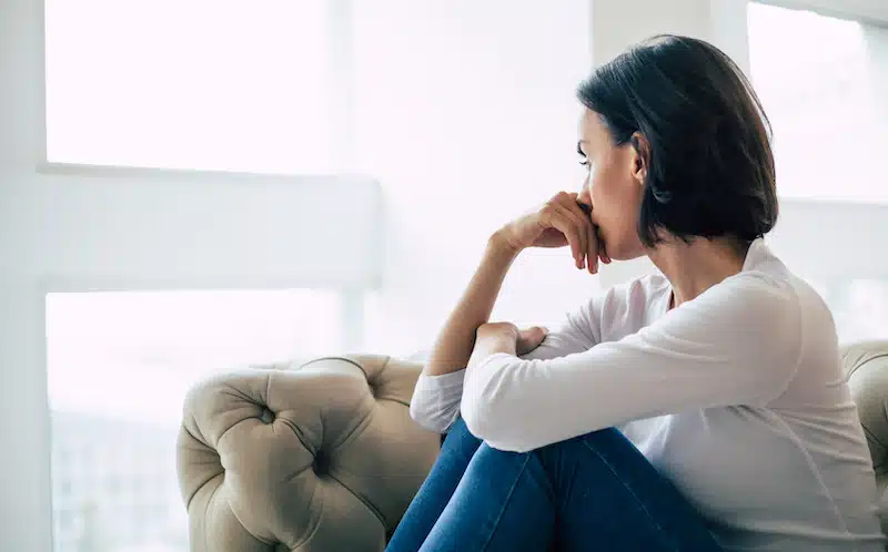 A woman sits on a couch and looks out the window.